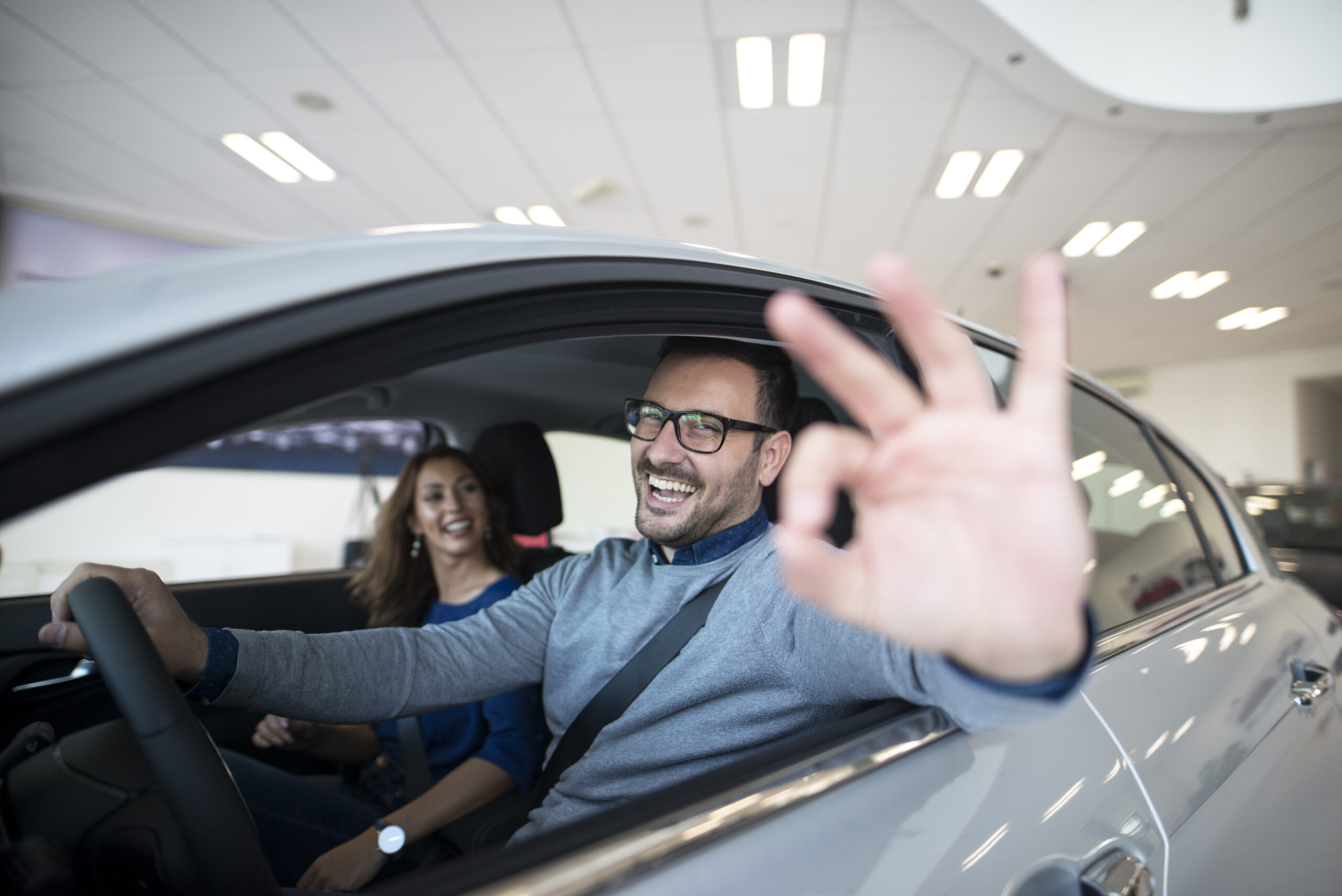 Casal comemorando compra de carro novo com cota contemplada de veículo, rapaz fazendo sinal de ok